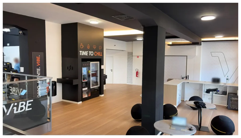 Ingresso e area lounge della palestra Vibe Fitness ad Arcore, con reception, sedute sferiche e area distributori con la scritta Time to Chill