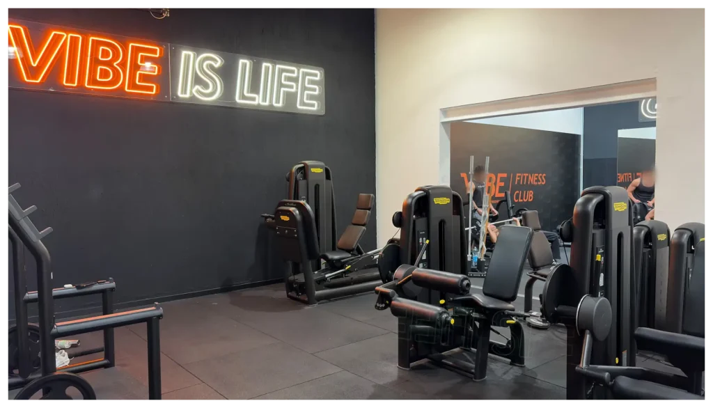 Macchinari isotonici per l'allenamento della parte inferiore del corpo nella palestra Vibe Fitness ad Arcore, con insegna al neon Vibe is Life