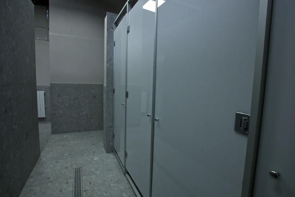 Cabine doccia moderne con finiture grigio effetto pietra e porte bianche negli spogliatoi della palestra ViBE Fitness ad Arosio.