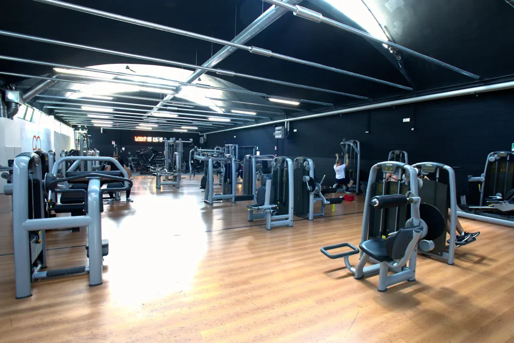 Panoramica della sala pesi con macchinari isotonici moderni e pavimentazione in parquet presso ViBE Fitness ad Arosio.