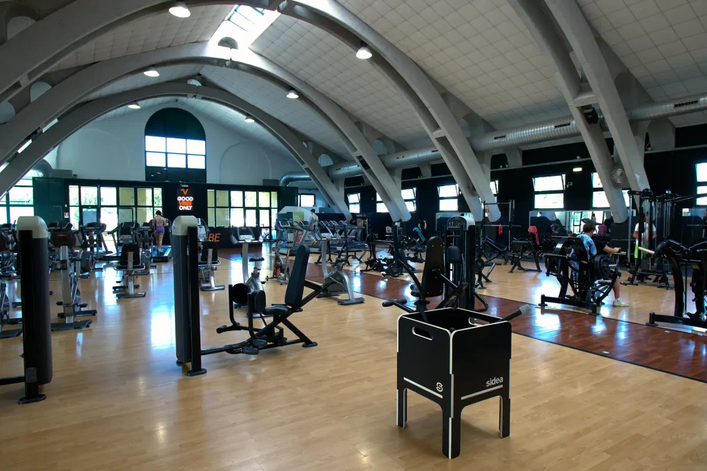 Ampia sala attrezzi di ViBE Fitness Barlassina caratterizzata da soffitto ad archi, macchinari isotonici e un rialzo Sidea in primo piano.