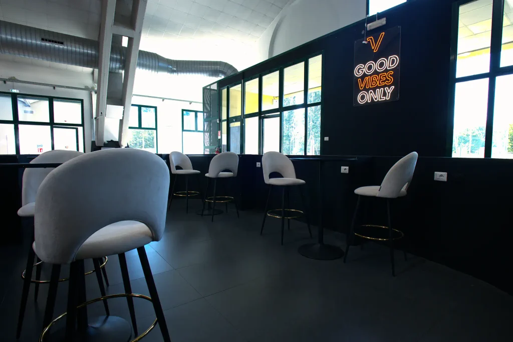 Zona relax di ViBE Fitness Barlassina con eleganti sgabelli bianchi, tavoli alti e la scritta a neon 