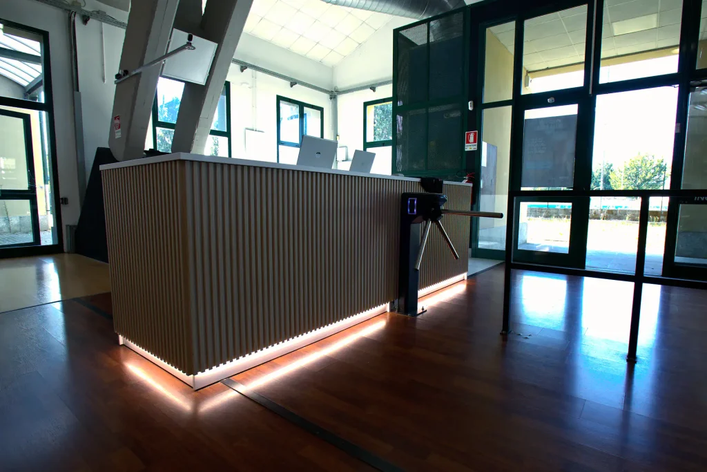 Ingresso con bancone reception in listelli di legno illuminato a LED e tornello di controllo accessi presso ViBE Fitness Barlassina.