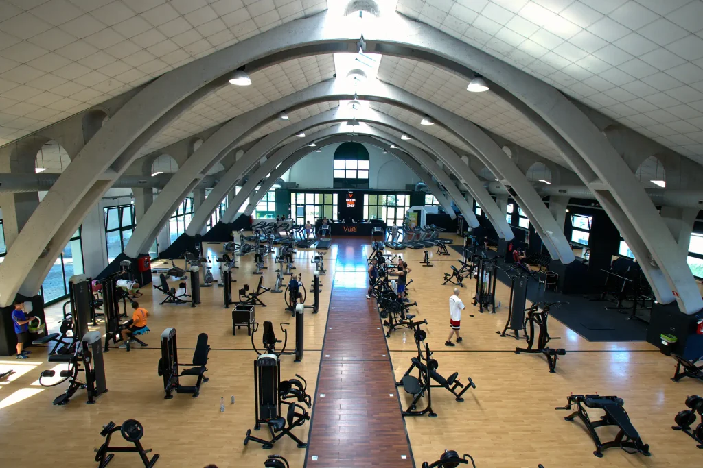 Inquadratura dall'alto che mostra l'intera estensione della sala attrezzi di ViBE Fitness a Barlassina sotto la caratteristica architettura ad archi.