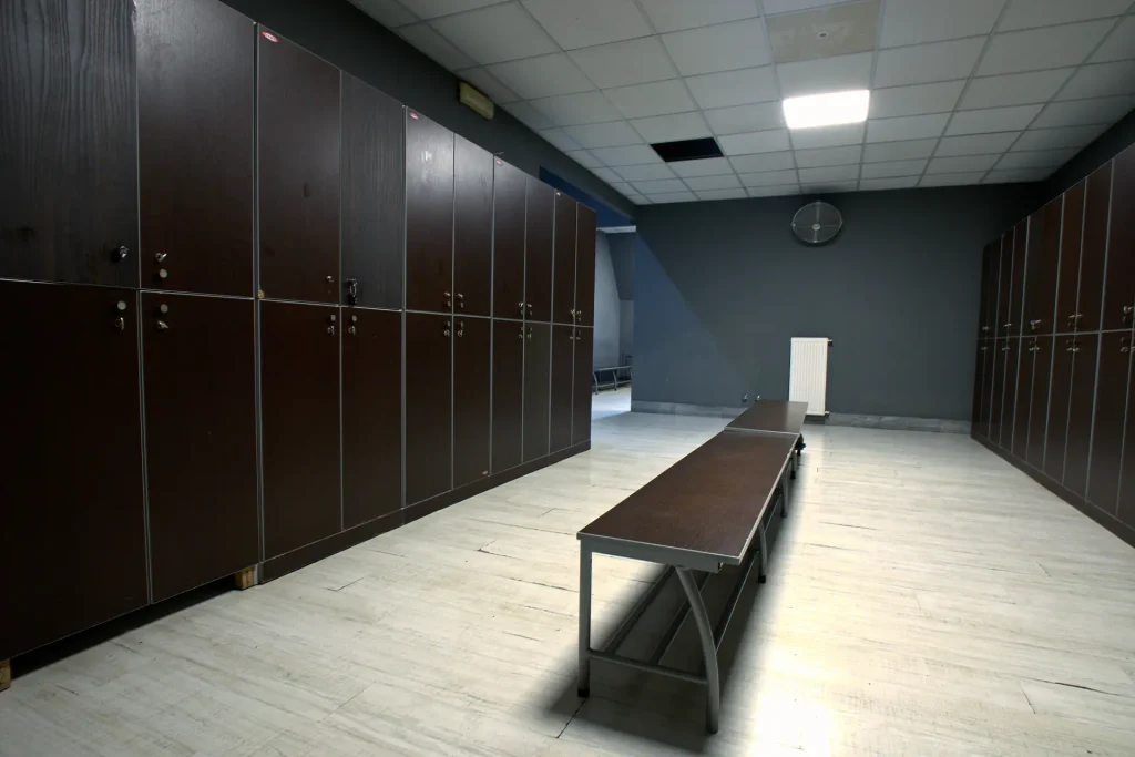 Interno dello spogliatoio della palestra ViBE Fitness a Barlassina, con ampie file di armadietti in legno scuro e panche centrali su pavimento in parquet chiaro.