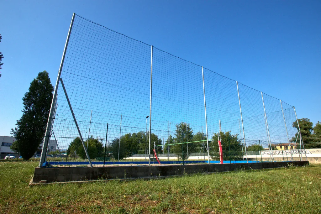 ampo da beach volley esterno con sabbia e rete di protezione alta, situato nell'area verde della palestra ViBE Fitness a Barlassina.