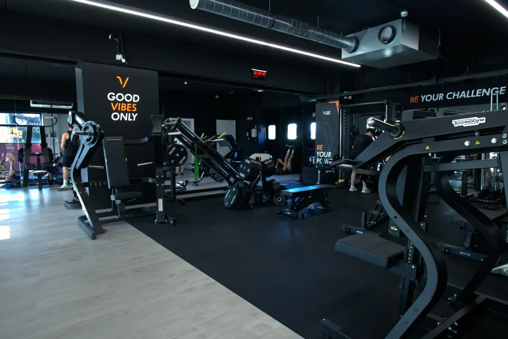 Zona allenamento isotonico di ViBE Fitness Lentate con macchinari per gambe e pettorali su pavimentazione gommata e grafiche 