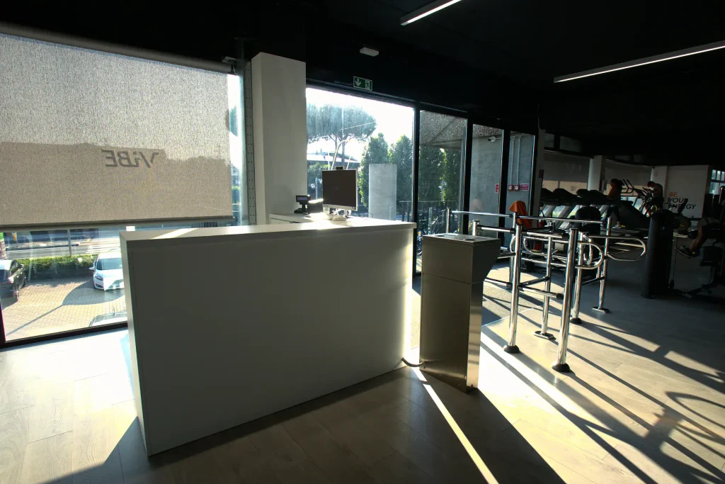 Bancone d'accoglienza bianco e tornello di controllo accessi presso l'ingresso illuminato di ViBE Fitness Lentate.