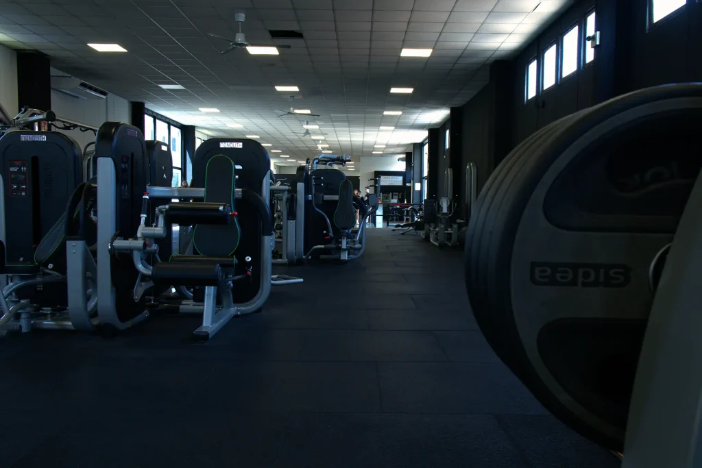 Inquadratura della sala attrezzi di ViBE Fitness Seregno con macchinari Monolith, disco bumper Sidea in primo piano e corridoio centrale verso l'area break.