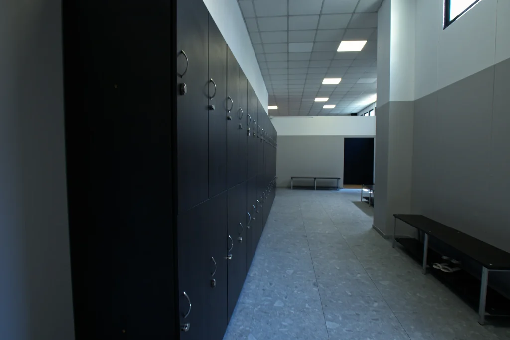 Corridoio interno dello spogliatoio di ViBE Fitness Seregno con ampie file di armadietti neri, panche e pavimento in piastrelle grigie.
