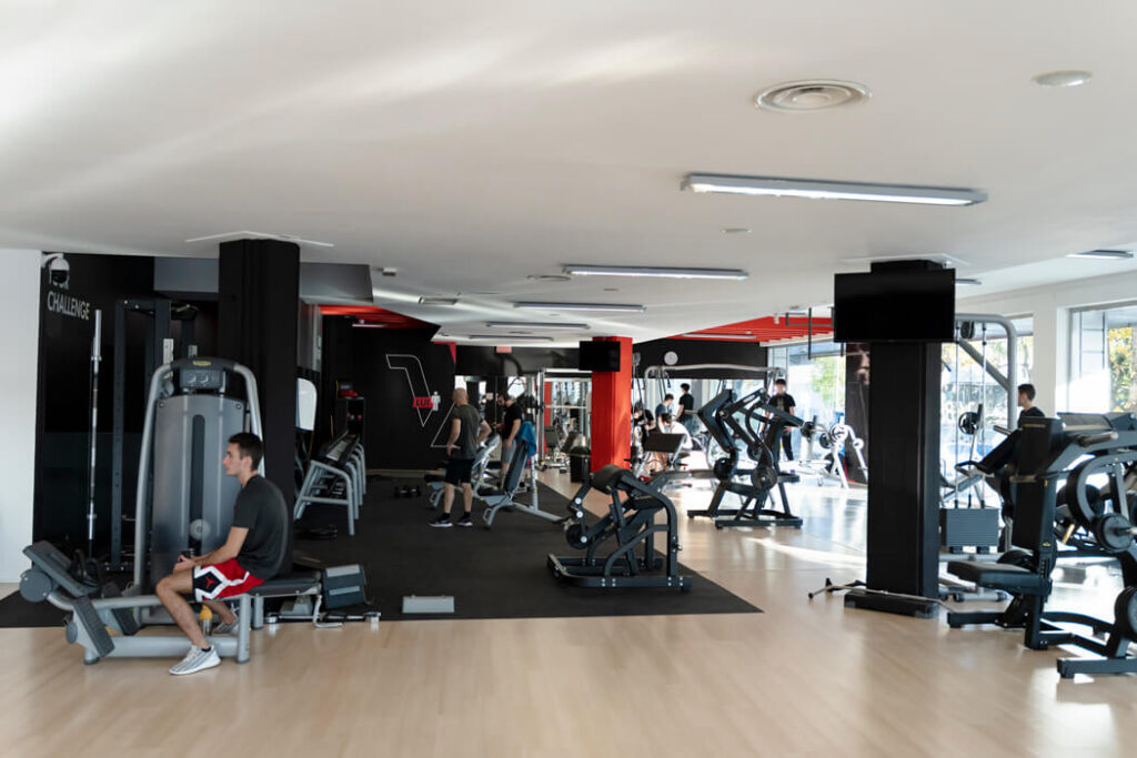 Vista interna dell'ampia sala pesi di Vibe Fitness Varedo con pavimentazione in parquet e gomma, macchinari isotonici e utenti durante l'allenamento.