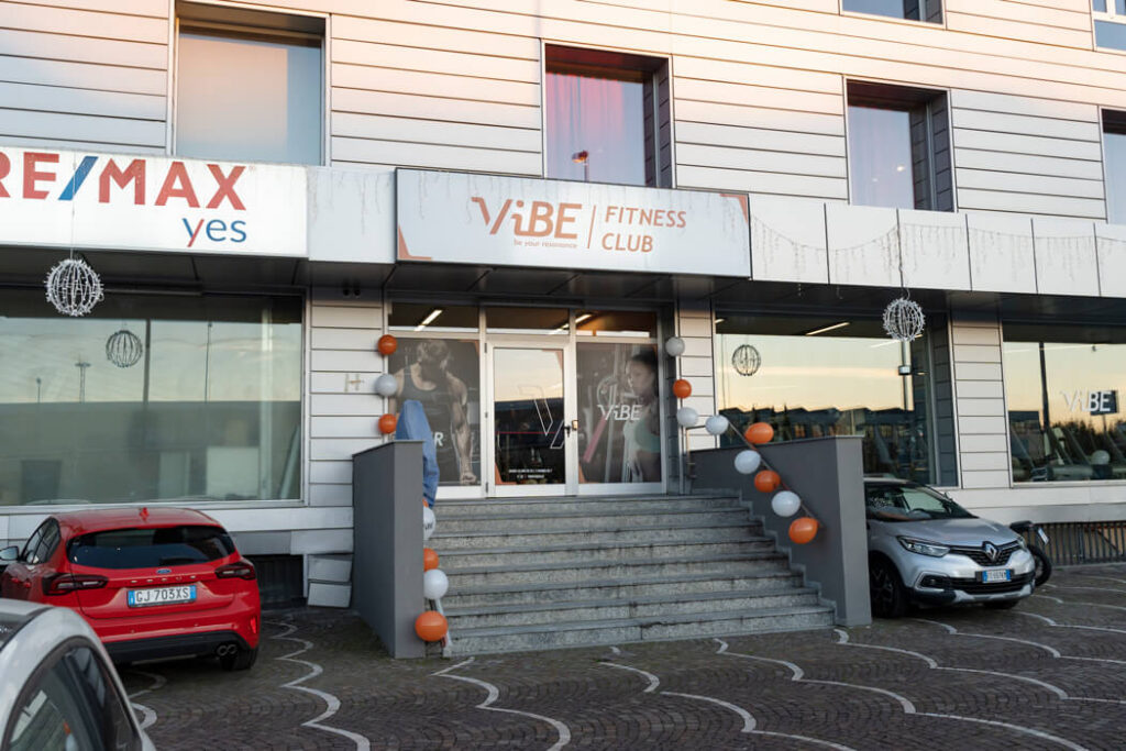 Insegna e ingresso principale di Vibe Fitness Club Varedo con scalinata in pietra decorata con palloncini arancioni e bianchi per l'inaugurazione.