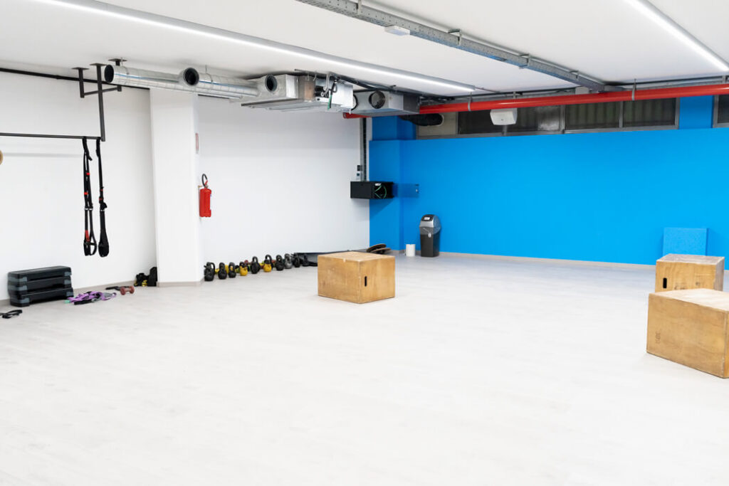 Ampia sala fitness con pareti blu brillante, specchi a tutta parete e attrezzature assortite come palle mediche, kettlebell e blocchi di legno su un pavimento in laminato chiaro.